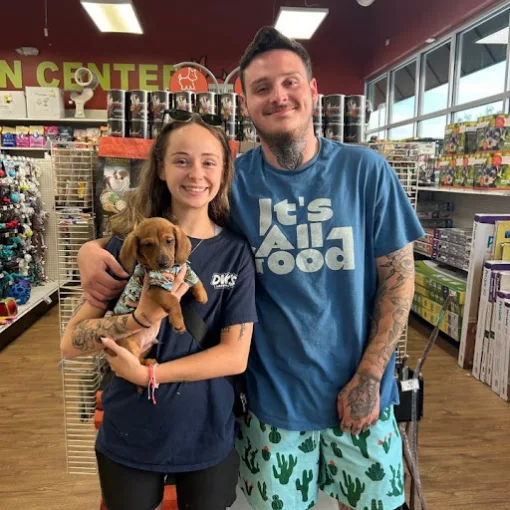 A smiling couple holding a small puppy in the store